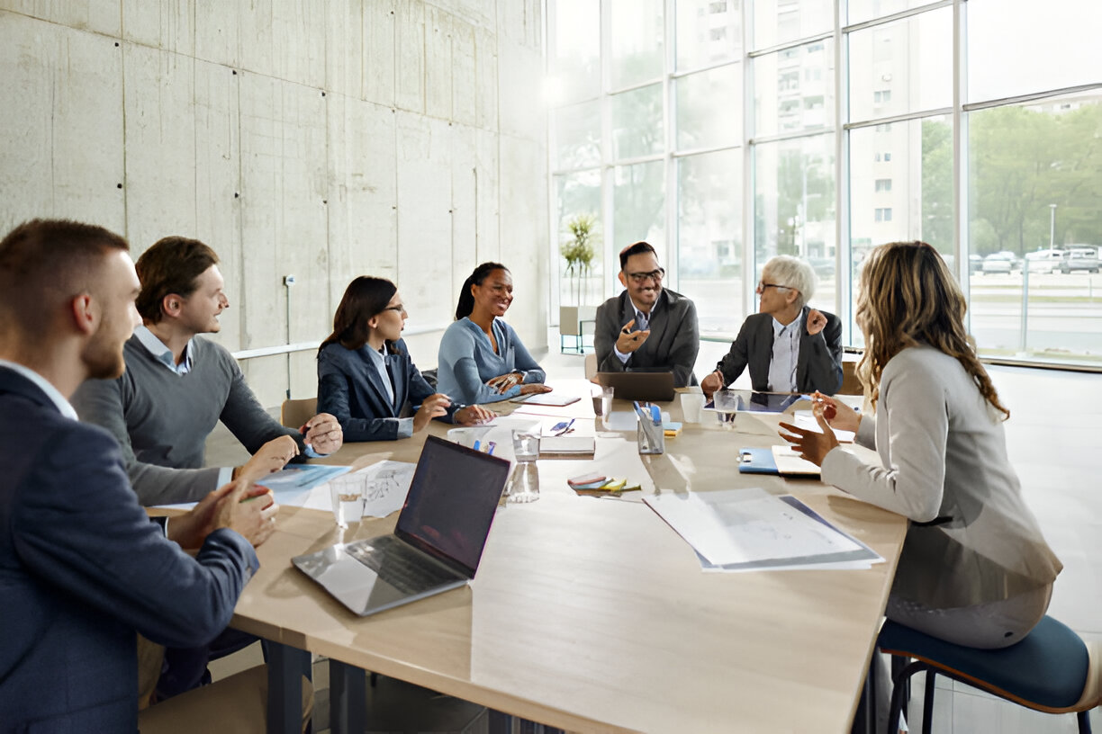 A diverse group of professionals engaged in a lively discussion around a conference table in a modern office setting.