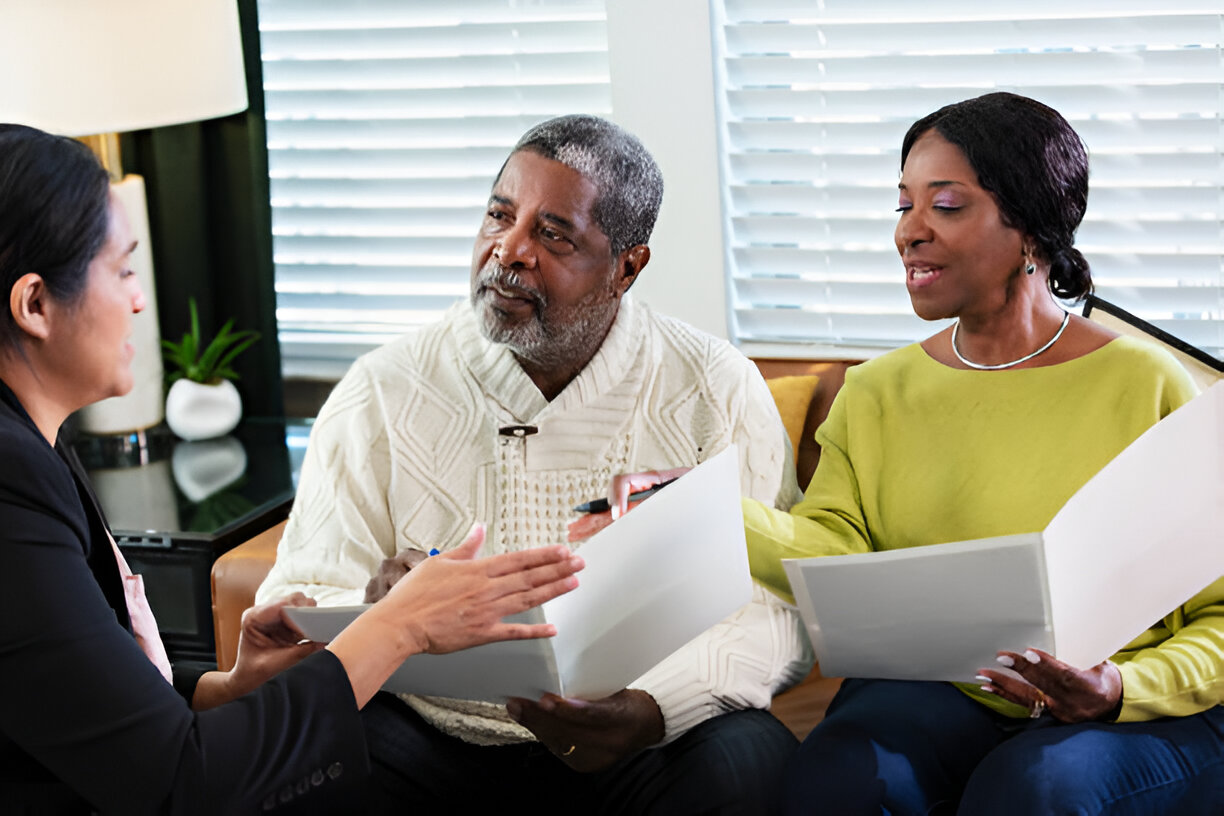 A financial advisor or consultant discussing documents with an older couple in a cozy, well-lit office setting.