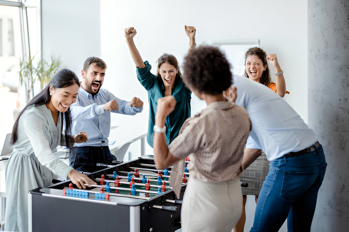 A group of excited coworkers playing foosball in an office, celebrating and cheering.
