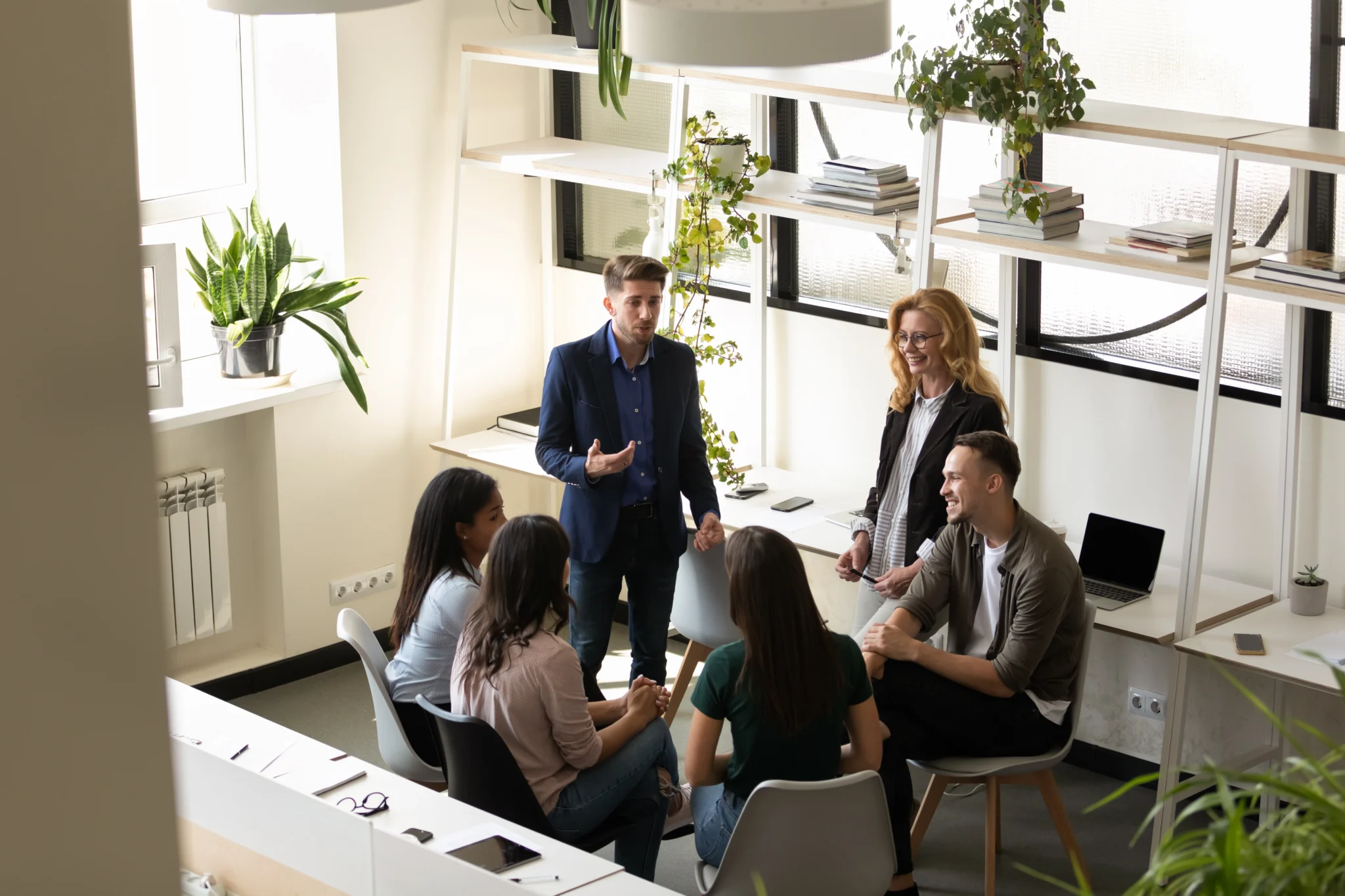 A group of diverse professionals engaged in a discussion in a modern office with natural light and plants.